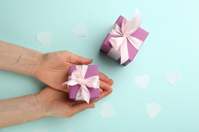 Photo of Woman holding gift box on turquoise background, top view. Valentine's Day celebration