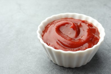 Bowl of tasty ketchup on light grey table, closeup. Space for text