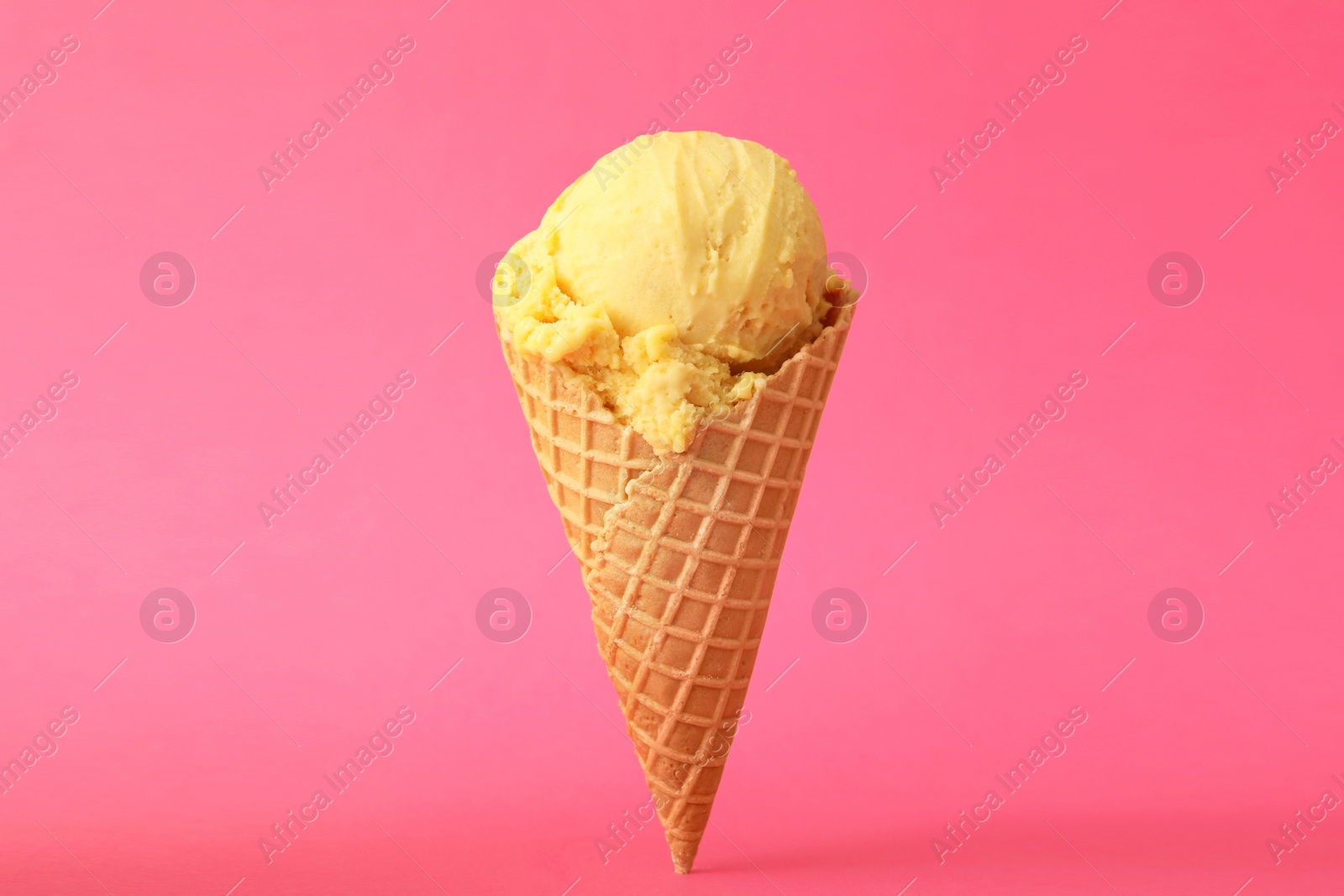 Photo of Delicious yellow ice cream in waffle cone on pink background