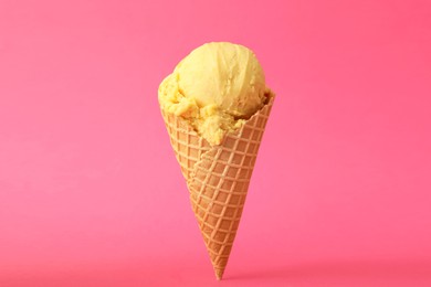 Photo of Delicious yellow ice cream in waffle cone on pink background