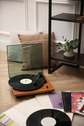 Stylish turntable with vinyl records on floor indoors
