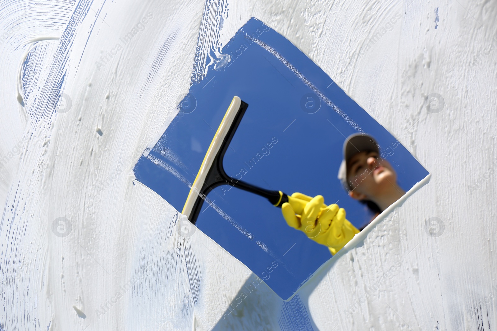 Photo of Woman cleaning glass with squeegee on sunny day