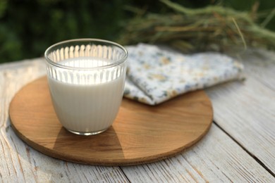 Photo of Glass of tasty fresh milk on white wooden table outdoors, space for text