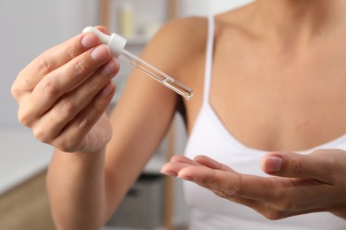 Woman applying cosmetic serum onto her finger on blurred background, closeup