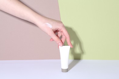 Woman with tube of cream on color background, closeup