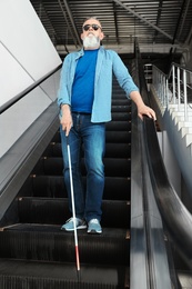 Blind person with long cane on escalator indoors