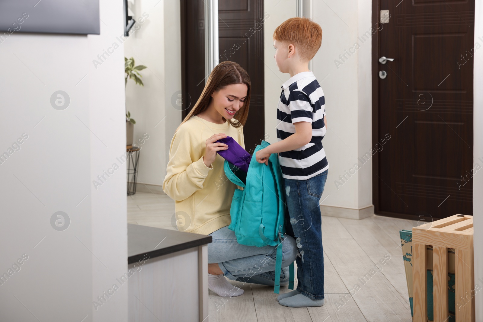 Photo of Young mom preparing her son for school at home