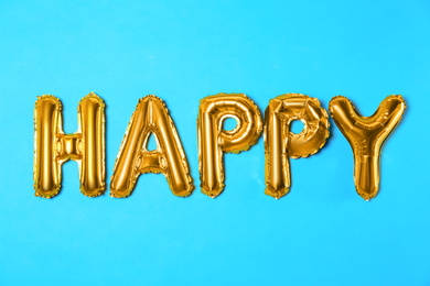 Photo of Word HAPPY made of golden foil balloon letters on light blue background