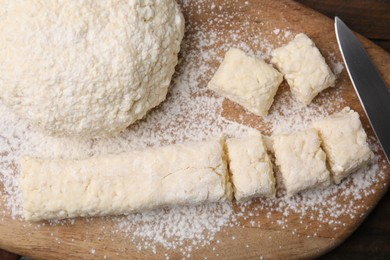 Photo of Making lazy dumplings. Wooden board with raw dough, flour and knife on table, flat lay