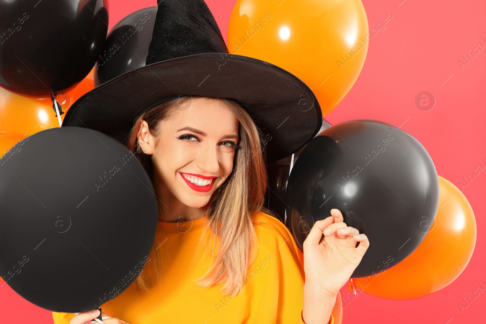 Photo of Beautiful woman wearing witch costume with balloons for Halloween party on red background