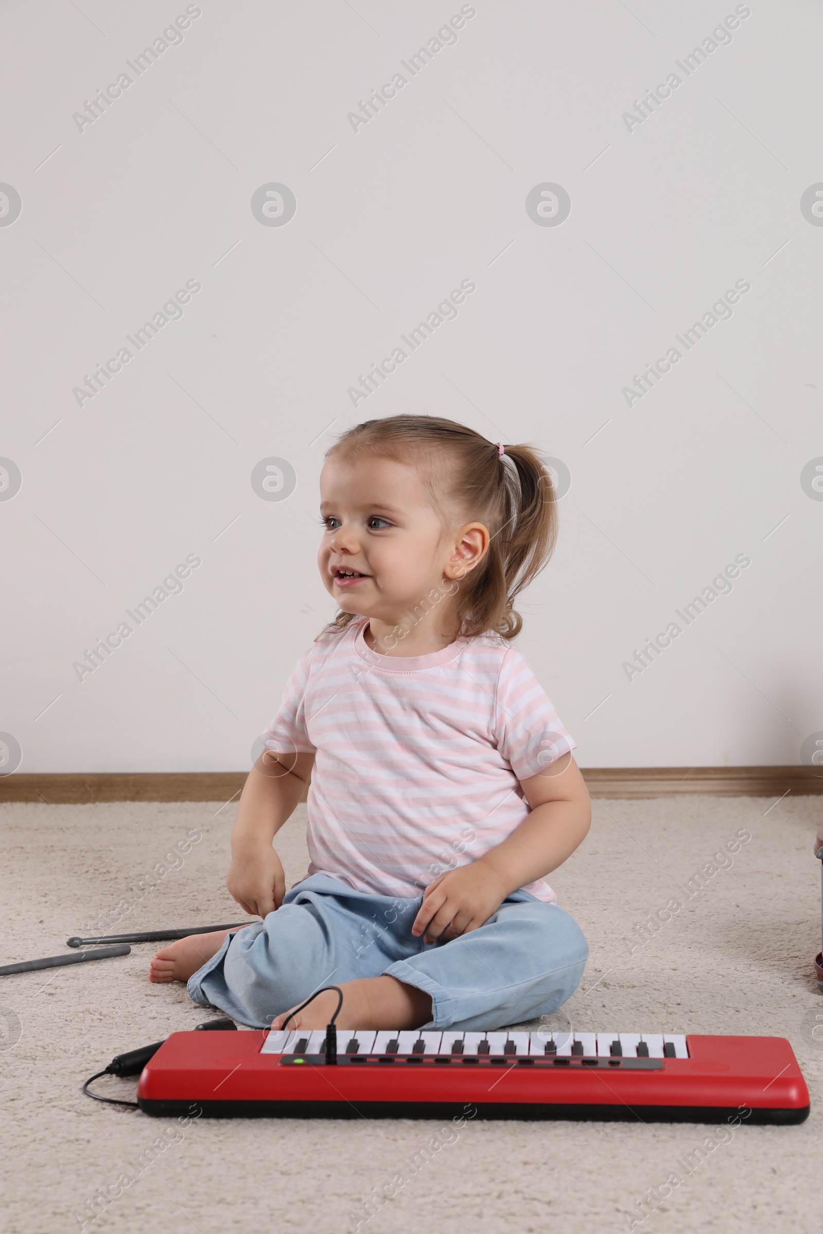 Photo of Cute little girl playing with toy piano at home