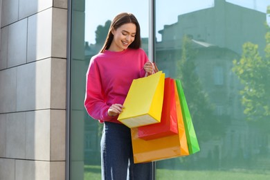 Photo of Beautiful young woman with shopping bags near building outdoors