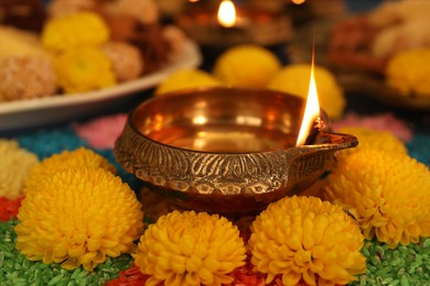 Diwali celebration. Diya lamp, colorful rangoli and chrysanthemum flowers on table, closeup