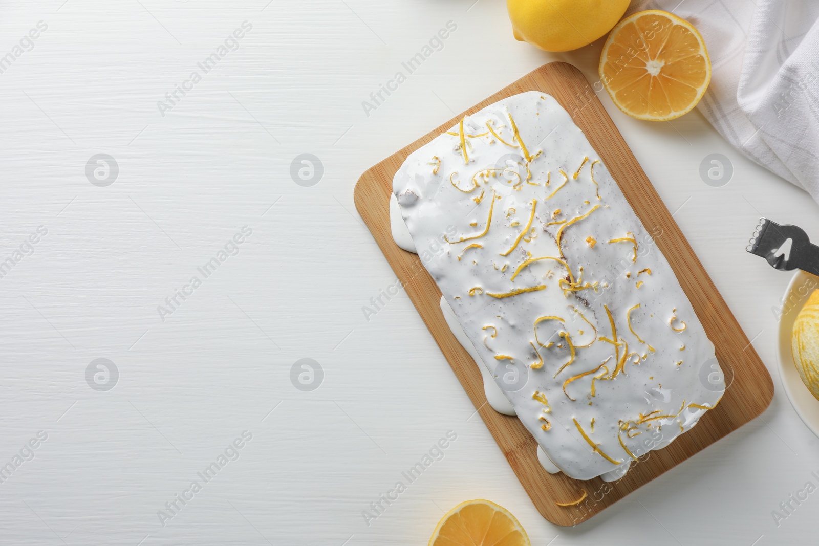 Photo of Tasty lemon cake with glaze and citrus fruits on white wooden table, flat lay. Space for text