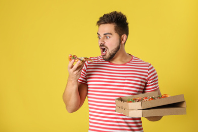 Photo of Emotional man with tasty pizza on yellow background