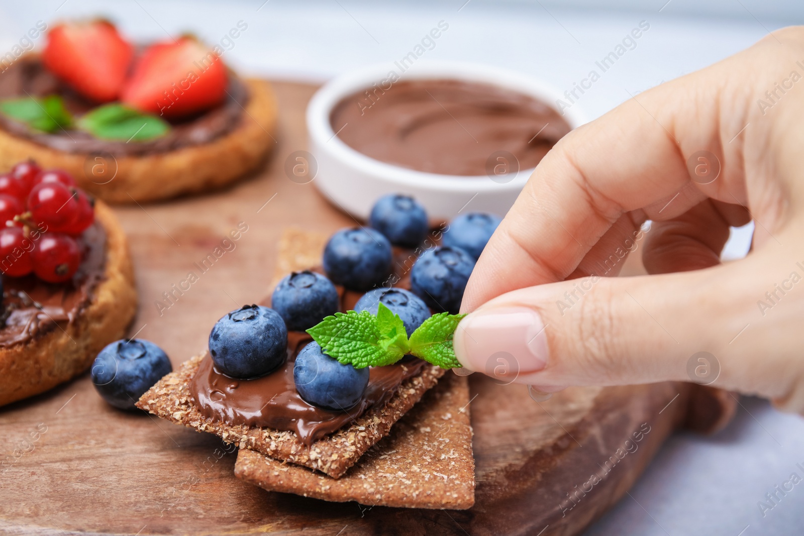 Photo of Woman decorating rye crispbreads with mint at table, closeup