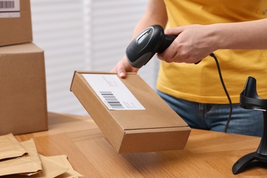 Photo of Parcel packing. Post office worker with scanner reading barcode at wooden table indoors, closeup