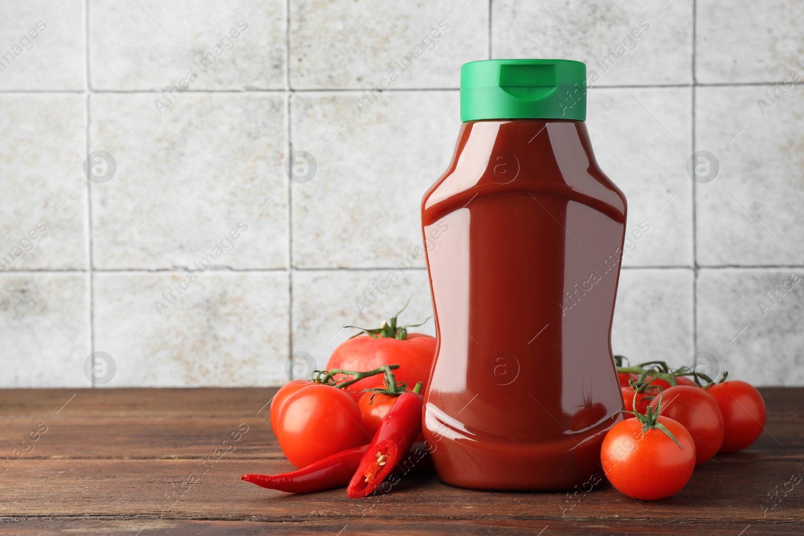 Photo of Bottle of tasty ketchup, tomatoes and chili pepper on wooden table. Space for text