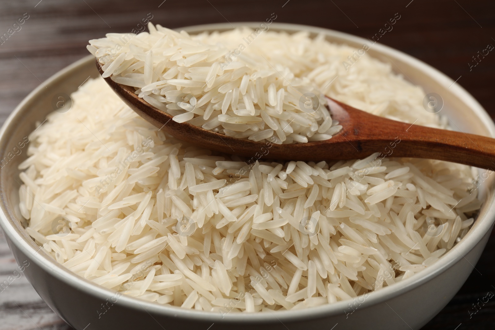 Photo of Raw basmati rice and wooden spoon in bowl on table, closeup