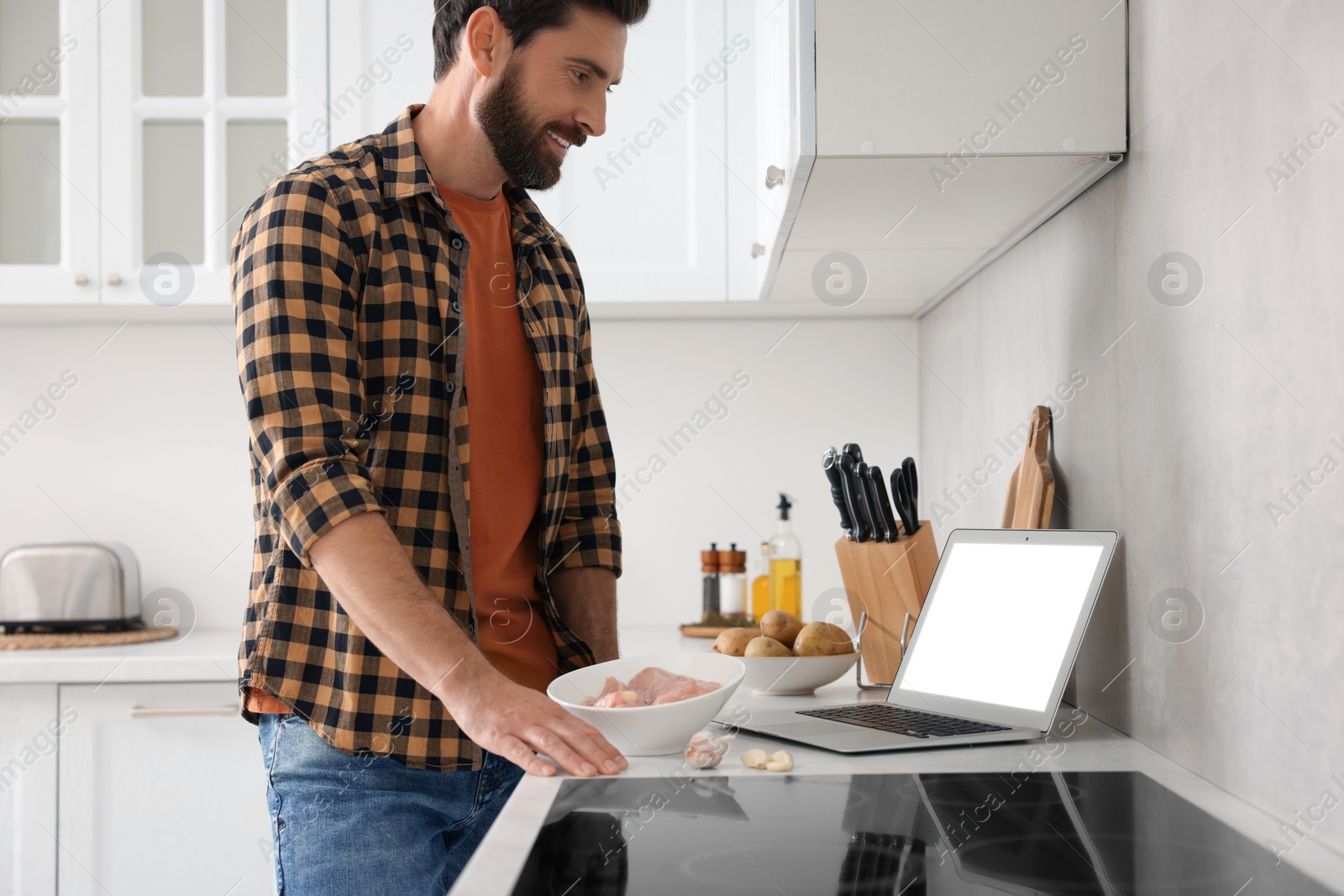 Photo of Man making dinner while watching online cooking course via laptop in kitchen