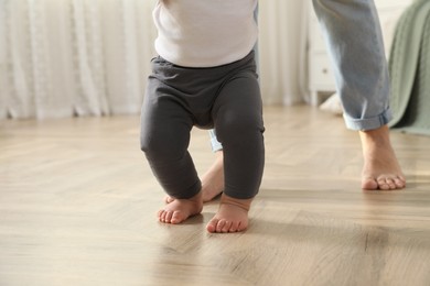 Photo of Mother supporting her baby daughter while she learning to walk at home, closeup