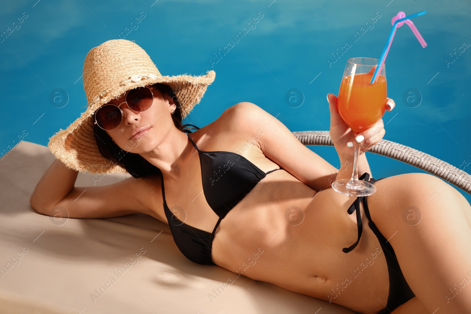 Photo of Young woman in stylish black bikini with cocktail near swimming pool