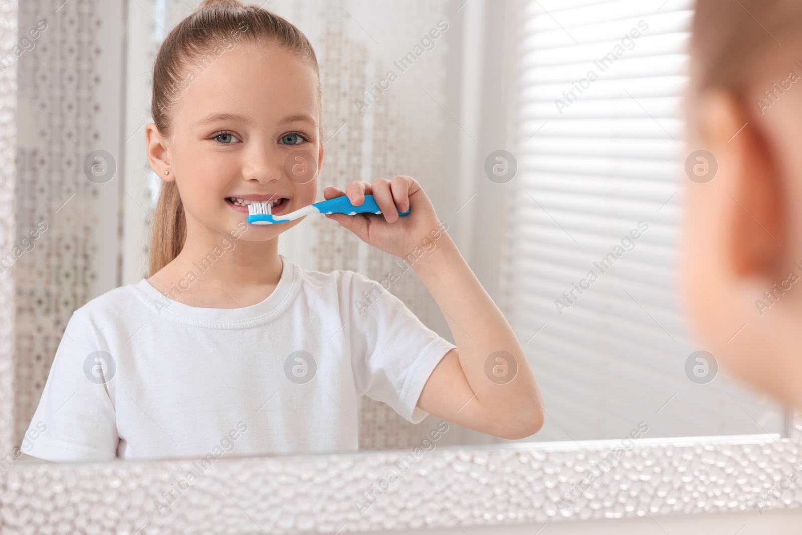 Photo of Cute little girl brushing her teeth with plastic toothbrush near mirror indoors