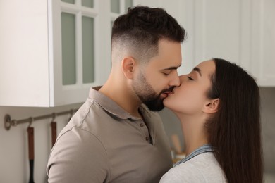 Photo of Affectionate young couple kissing in light kitchen