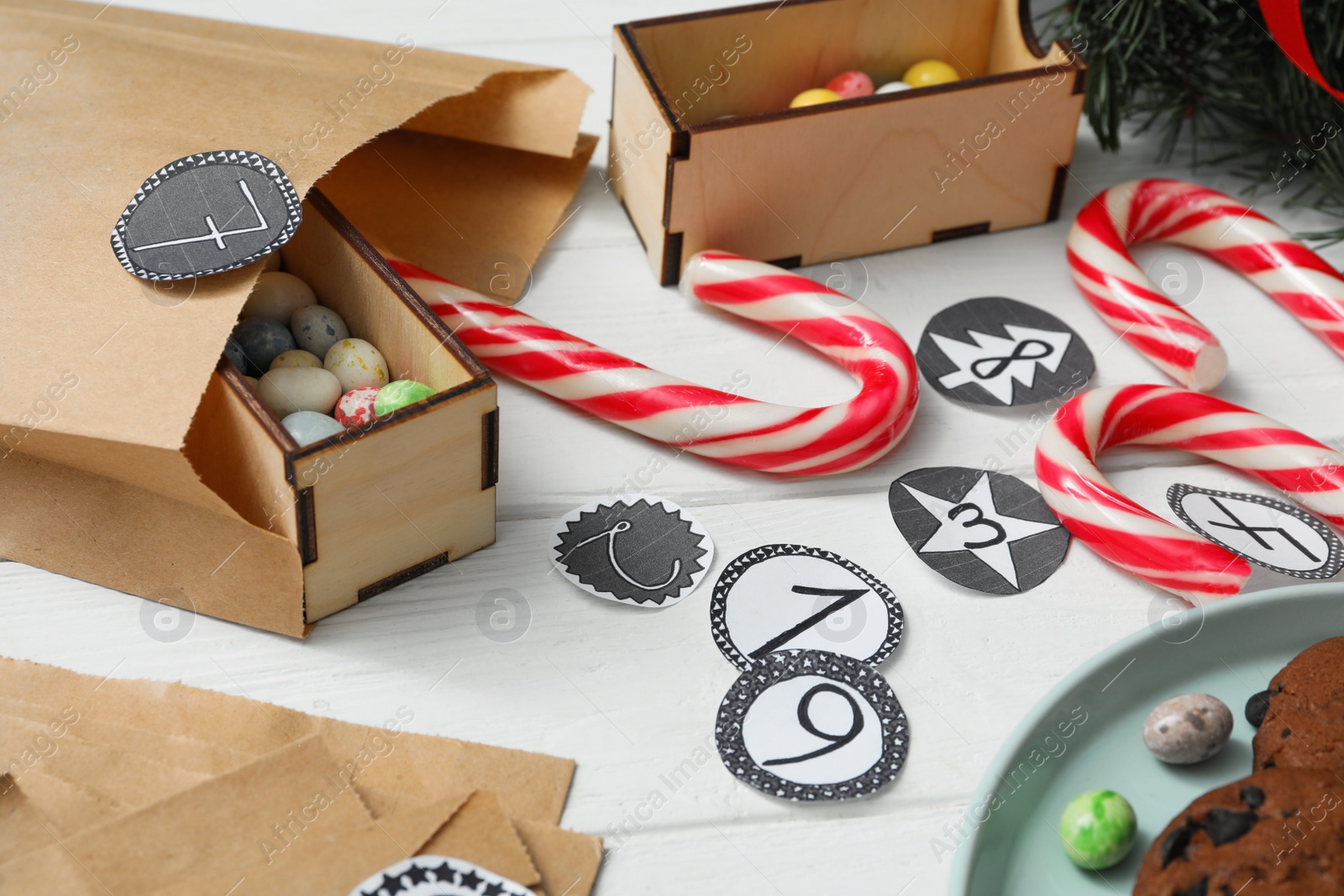 Photo of Paper bag and treats on white wooden table, closeup. Creating advent calendar