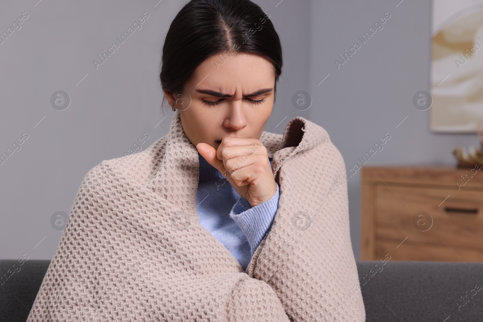 Photo of Woman wrapped in blanket coughing at home. Cold symptoms