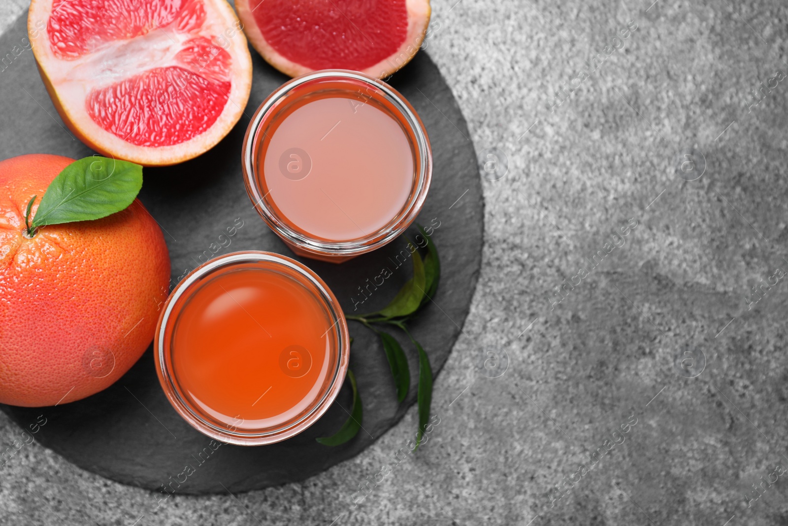 Photo of Tasty freshly made grapefruit juice and fruits on grey table, flat lay. Space for text