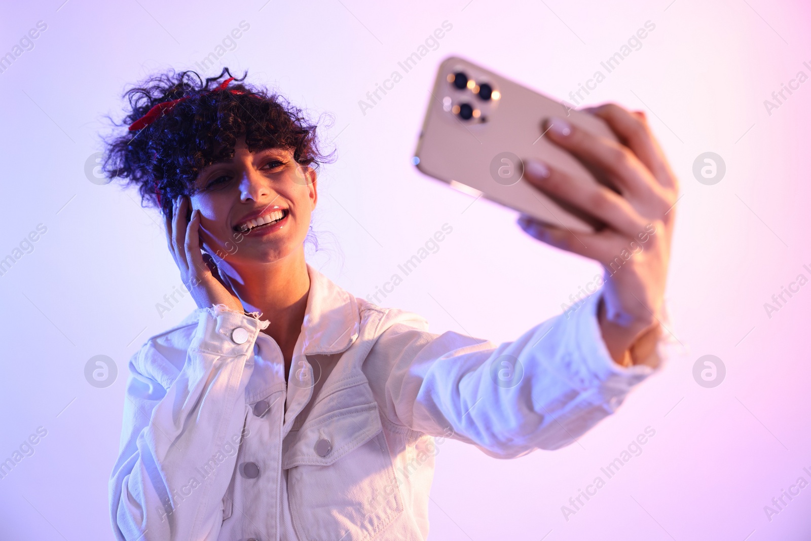 Photo of Beautiful young woman taking selfie on color background in neon lights