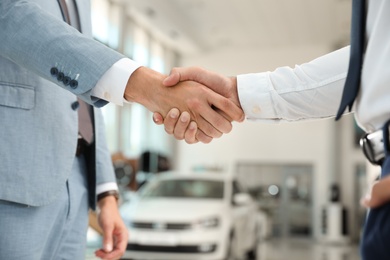 Young salesman shaking hands with client in modern car dealership, closeup