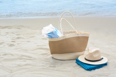 Photo of Bag with blanket, beach towel and straw hat on sandy seashore, space for text