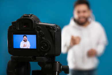 Photo of Young blogger shooting video with camera against blue background, focus on screen