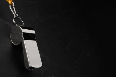 Referee equipment. Metal whistle on black textured background, closeup and space for text