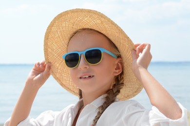 Little girl wearing sunglasses and hat at beach on sunny day