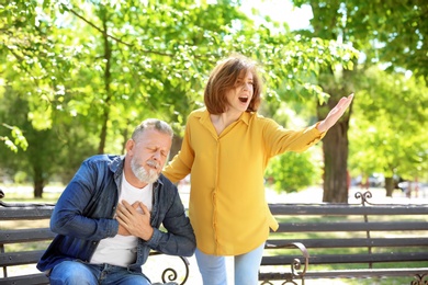 Woman helping mature man suffering from heart attack on bench in park