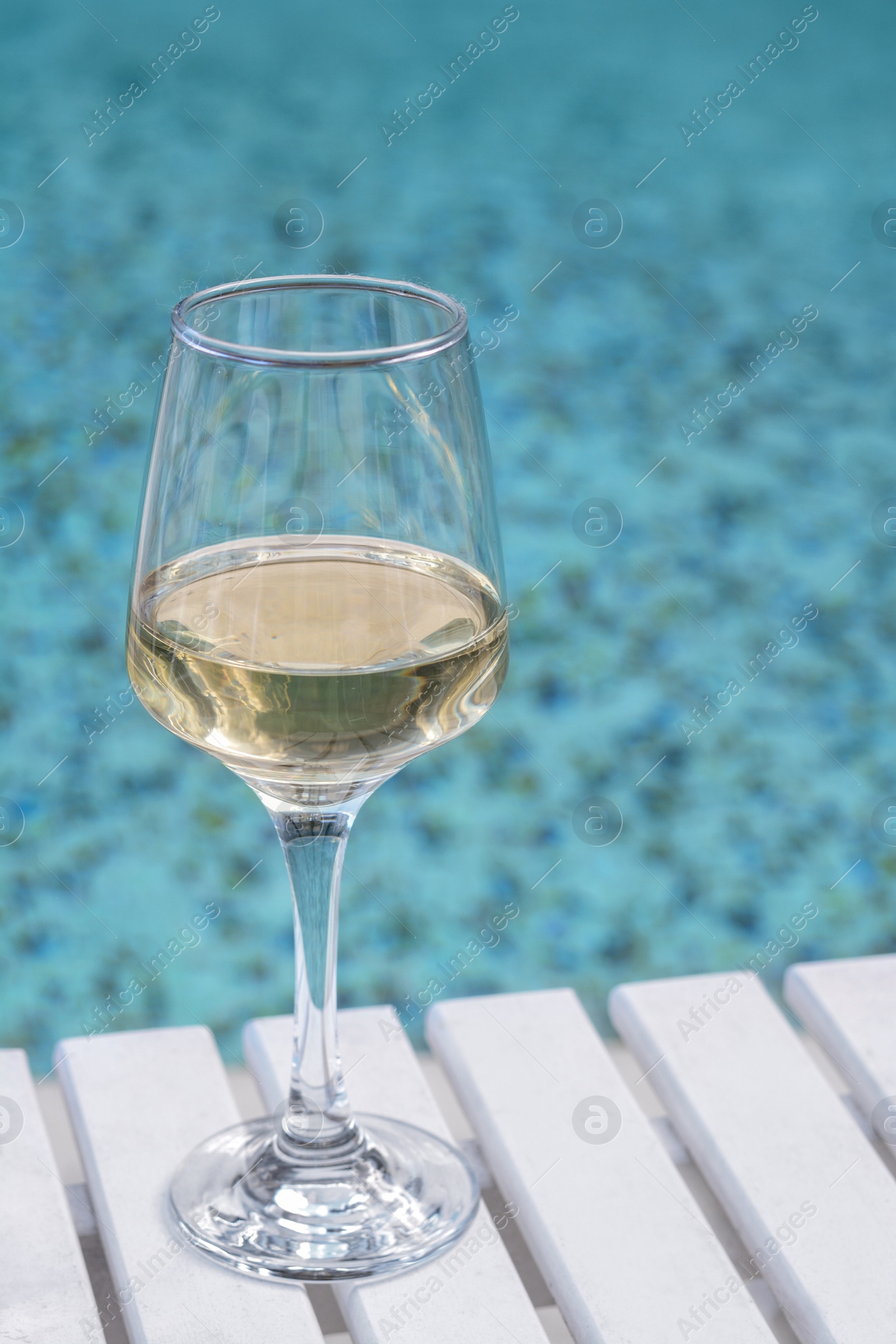 Photo of Glass of tasty wine on wooden table near swimming pool