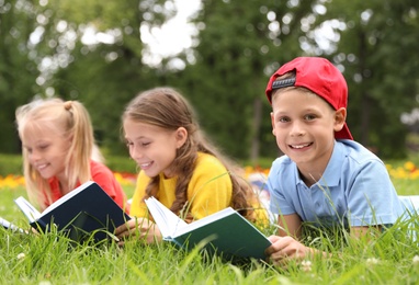 Group of little children reading books on green grass in park