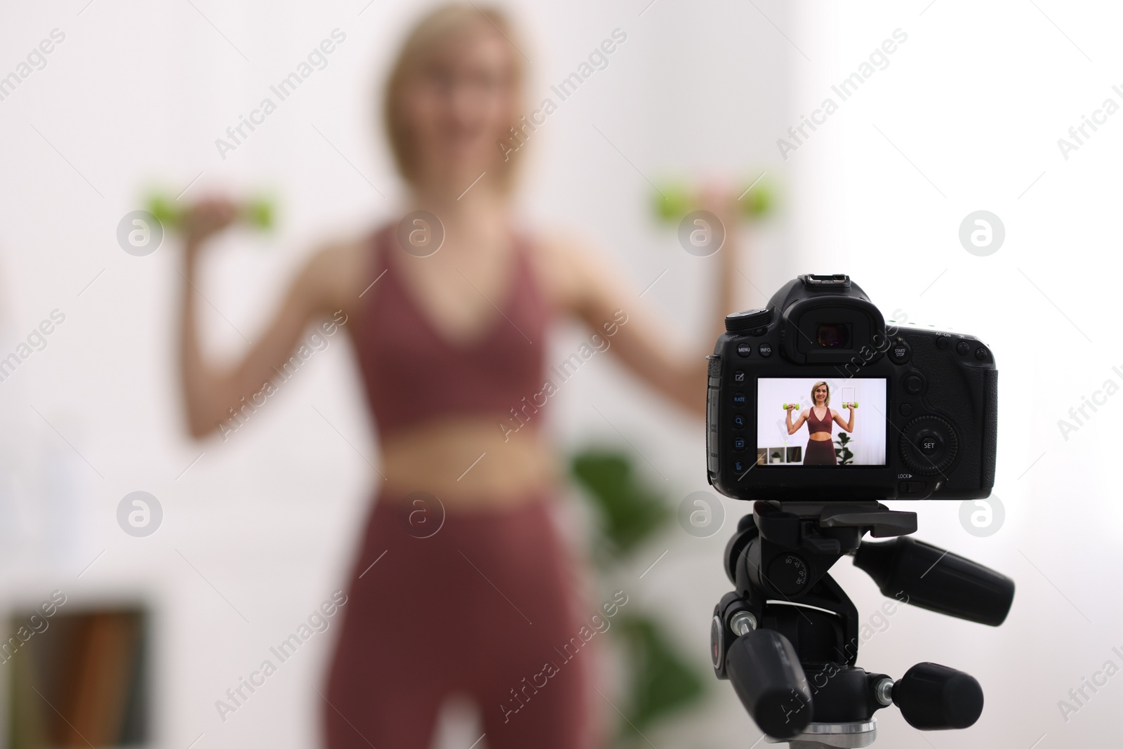 Photo of Smiling sports blogger working out with dumbbells while recording fitness lesson at home, focus on camera. Space for text