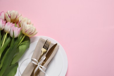 Stylish table setting with cutlery and tulips on pink background, flat lay. Space for text