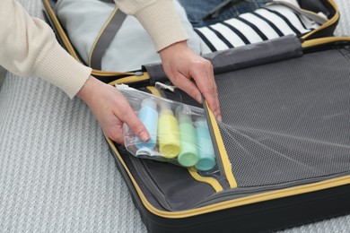 Photo of Woman with plastic bag of cosmetic travel kit packing suitcase, closeup. Bath accessories