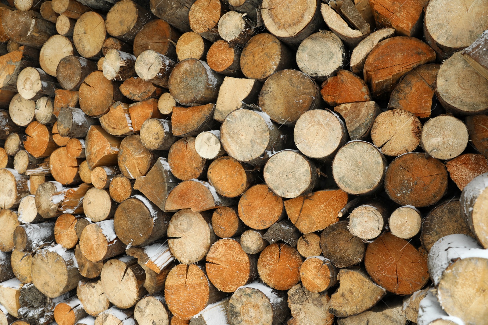 Photo of Stacked firewood with snow as background, closeup. Heating house in winter