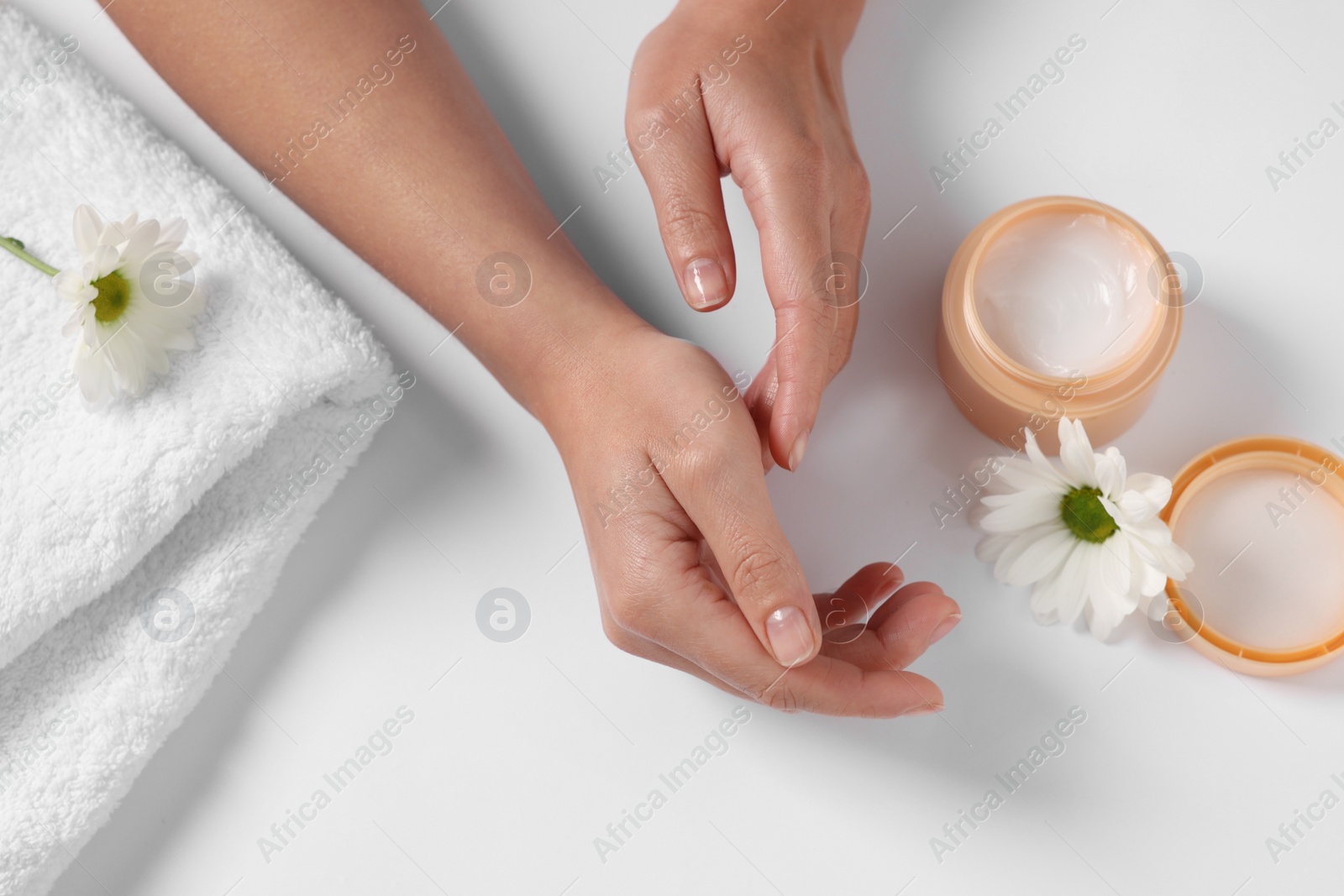 Photo of Woman with jar of hand cream, towel and chamomile flowers on white background, top view