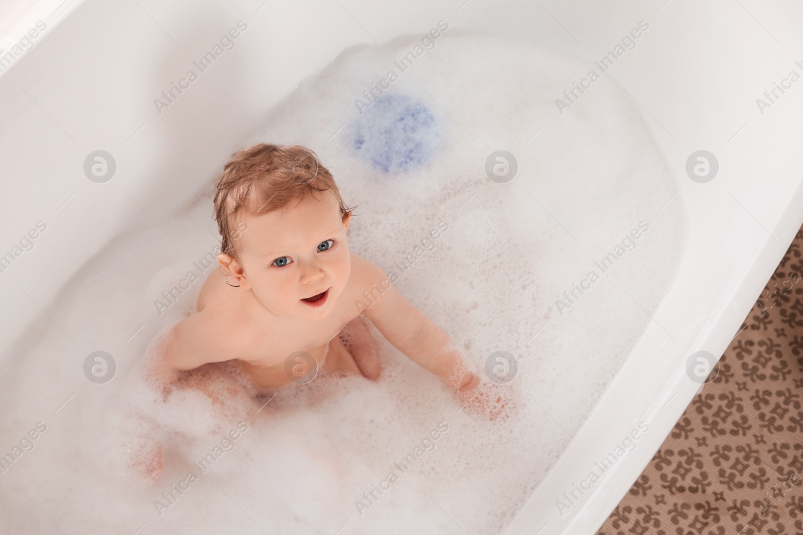 Photo of Cute little baby bathing in tub at home, top view