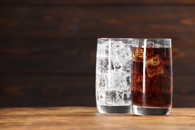 Photo of Glasses of different refreshing soda water with ice cubes on wooden table, space for text