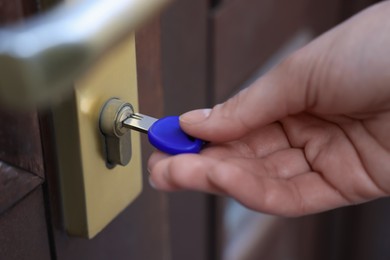 Photo of Woman opening door with key outdoors, closeup