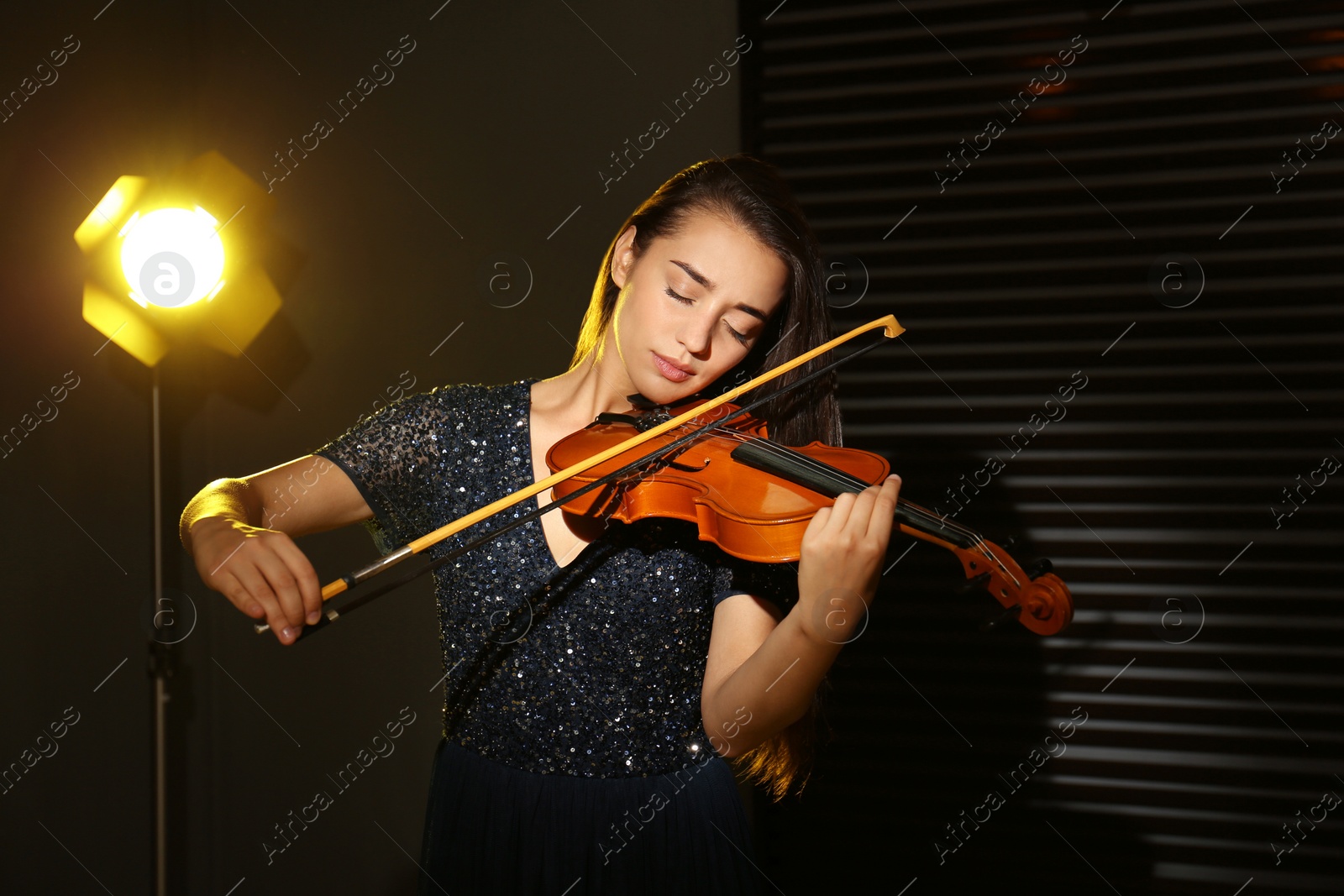 Photo of Beautiful young woman playing violin in dark room