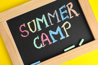 Blackboard with words SUMMER CAMP and colorful chalk on yellow background, closeup